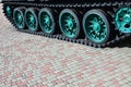 A military vehicle on caterpillar tracks stands on a square of paving stones. Photo of green caterpillars with metal wheels that Royalty Free Stock Photo