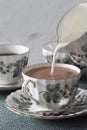 Milk being poured into a cup of tea in a porcelain tea set on a green placemat