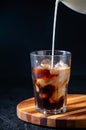 Milk Being Poured into Iced Coffee in Tall Glass on Dark Background. Concept Refreshing Summer Drink Royalty Free Stock Photo