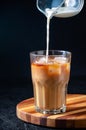 Milk Being Poured into Iced Coffee in Tall Glass on Dark Background. Concept Refreshing Summer Drink Royalty Free Stock Photo