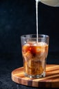 Milk Being Poured into Iced Coffee in Tall Glass on Dark Background. Concept Refreshing Summer Drink Royalty Free Stock Photo