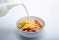 Milk being poured out of a jar into a bowl of cereal and strawberries on a white background