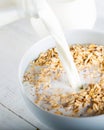 Milk being poured over a bowl full of cereal on wooden background