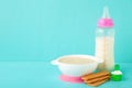 Milk and bowl with porridge for baby on blue background