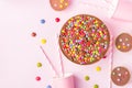 Milk Chocolate Birthday Cake with Multicolored Glazed Candy Sprinkles Buttercups Paper Drinking Cups Pink Straws Pink Background