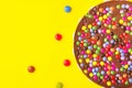 Milk chocolate birthday cake with multicolored glazed candy sprinkles decoration on bright yellow background. Kids party