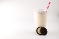 Milk with cookies in a glass with a pink straw, next to which is chocolate cream cookie cut in half on an isolated white