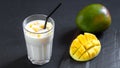 Milk drink on black background with mango. A classic mango milkshake - Lassi. A traditional drink in India from the heat