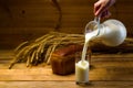 Milk from a glass jug poured into a glass, a loaf of rye bread, ears of corn Royalty Free Stock Photo