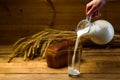 Milk from a glass jug poured into a glass, a loaf of rye bread, ears of corn Royalty Free Stock Photo