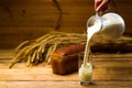 Milk from a glass jug poured into a glass, a loaf of rye bread, ears of corn Royalty Free Stock Photo