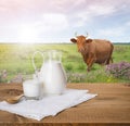 Milk jug and glass on wooden table over cow meadow Royalty Free Stock Photo