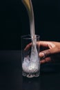 Milk pour into glass hold by black hand, closeup