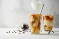 Milk is poured into coffee with ice on a light background. Two transparent glasses of refreshing iced coffee on a white Royalty Free Stock Photo