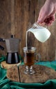 Milk is poured into decanter coffee. Geyser coffee maker, creamer on a wooden table. Glass cup with coffee making