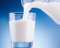 Milk poured from jug into glass on blue background Royalty Free Stock Photo