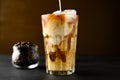 Milk is poured into a transparent glass with iced coffee on a black table. Royalty Free Stock Photo