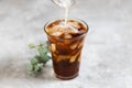 Milk is pouring into a tall glass with brew black coffee with pieces of ice on a gray dark background. Ice summer fresh coffee Royalty Free Stock Photo