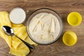 Milk, spoon on napkin, flour mixture with pieces of butter for muffins in bowl, silicone molds on table. Top view