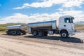 Milk tanker with a trailer stationary along a gravel road on a sunny day