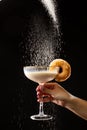 Milkshake glass and donut on black background. Powdered sugar falls