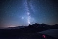 Milky way galaxy stars in the night sky over the Alps, illuminated camping tent in foreground, snowcapped mountain range, astro