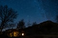 Milky way night sky starts are seen on a little house with lights on at night over mountains and trees. starry sky over scenic