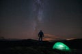 Milky way and starry sky over night scene outdoors in the forest and the mountains with green tent and silhouette of man infront. Royalty Free Stock Photo