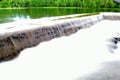 Milky white river water flowing over concrete barrier with lush summer forest