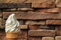 Milky White Vanilla Soft Serve Ice Cream Cone with Blurred Dark Brown Stone Blocks Wall in Background Royalty Free Stock Photo