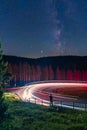 Milkyway, long exposure of a man standing at a railing in front of a curvy street, while cars are passing by and leave