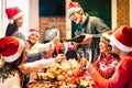 Millenial friends on santa hats celebrating Christmas with champagne and sweets food at log cabin - Winter holidays concept Royalty Free Stock Photo