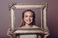 Millenial young woman blonde hair holds gilded picture frame in hands face portrait