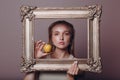 Millenial young woman blonde hair holds gilded picture frame in hands face portrait