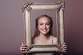 Millenial young woman blonde hair holds gilded picture frame in hands face portrait