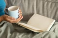 Millennial african american curly female reading book, enjoy relax and cup of tasty tea on sofa in room