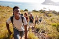 Millennial African American man leading friends hiking single file uphill on a path by the coast