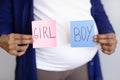 Millennial african american pregnant lady with big belly shows boy or girl paper on gray wall background