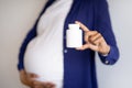 Millennial african american pregnant woman with big belly shows jar of vitamins pills on gray wall background