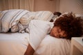 Millennial African American woman lying on her front asleep in bed, her partner in the background Royalty Free Stock Photo