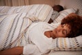 Millennial African American woman lying on her back asleep in bed, her partner in the background Royalty Free Stock Photo