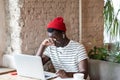 Millennial Afro-American man wear wireless headphones, holding glasses, rubbing his eyes, feels tired after working on laptop in Royalty Free Stock Photo