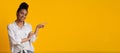 Millennial afro girl pointing aside at copy space on yellow background