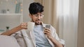 Millennial arabic guy indian handsome 30s man sitting at home on couch drinking hot tea coffee cappuccino cocoa from cup Royalty Free Stock Photo