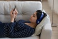 Millennial Asian girl in headphones relax on sofa with smartphone Royalty Free Stock Photo