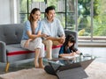 Millennial Asian happy family father and mother sitting on cozy sofa couch holding remote watching television while little young Royalty Free Stock Photo