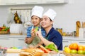 Millennial Asian little young boy chef wearing tall white cook hat and apron standing smiling holding sliced tomato posing Royalty Free Stock Photo