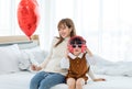 Millennial Asian young beautiful mother sitting on bed smiling holding red heart shaped air balloon while little cute preschooler Royalty Free Stock Photo