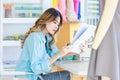 Millennial Asian young cheerful professional female dressmaker designer seamstress sitting smiling working alone holding looking Royalty Free Stock Photo