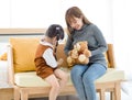 Asian young female mother sitting on cozy sofa smiling holding teddy bear doll playing doctor patient with little cute daughter gi